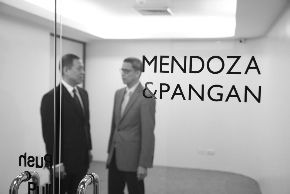Mendoza & Pangan partners talking behind glass pane with logo.